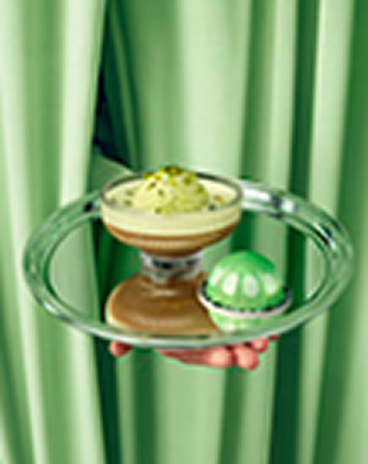 Pistachio coffee dessert and green capsule on a silver tray in front of green curtains